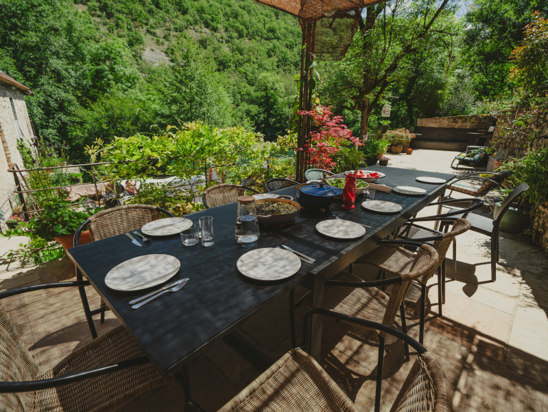 a dining table laid up for lunch on a terrace above a river in the south of France