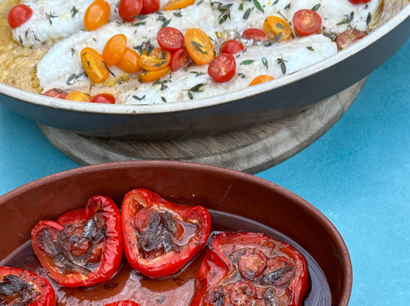 Two dishes with some roasted peppers in the foreground, and some baked fish in the background